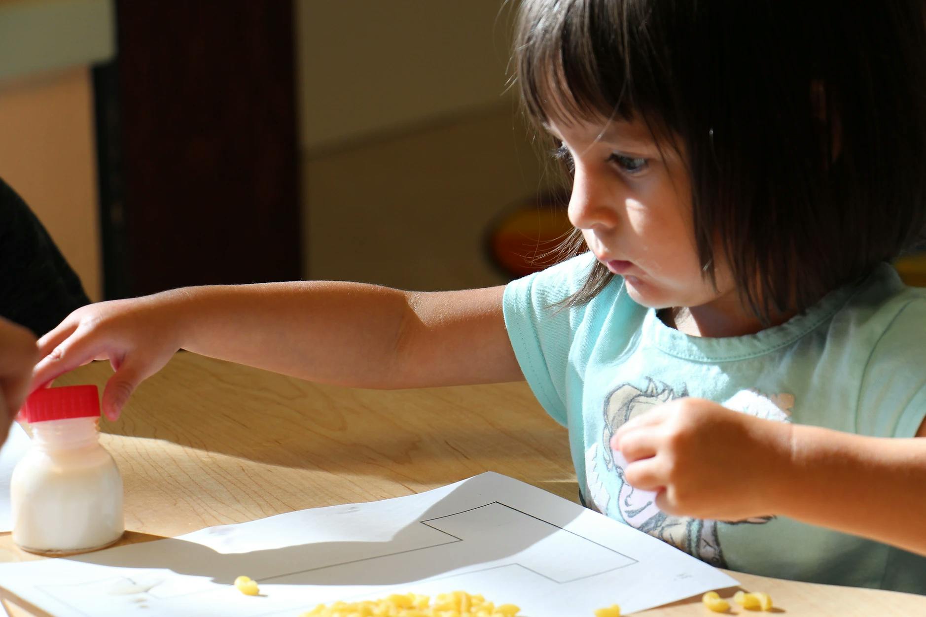 Child reaching for a small bottle while looking at a paper