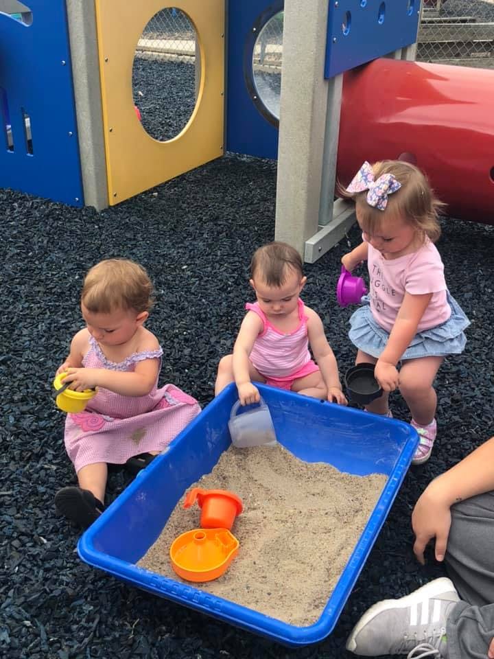 Three children playing with sand in a blue sandbox on a playground