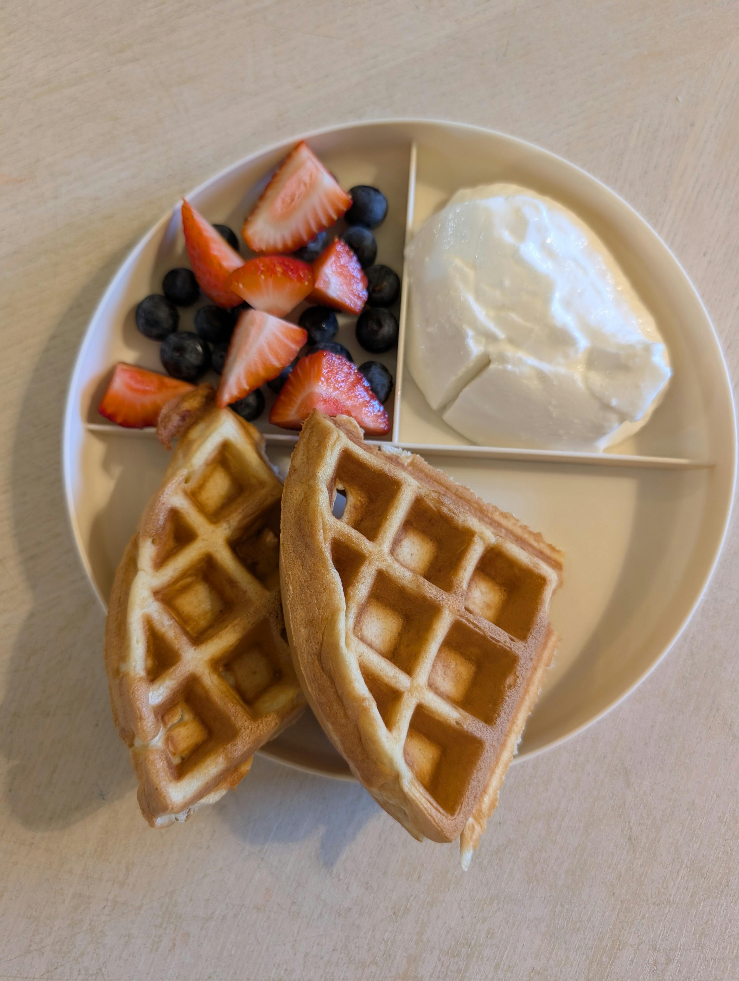 Plate with waffles, sliced strawberries, blueberries, and yogurt