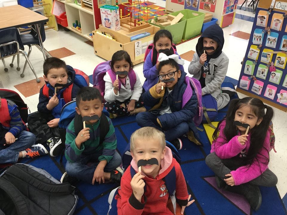 Group of children sitting on the floor with fake mustaches