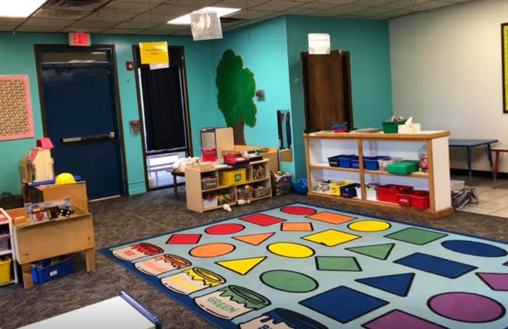 Classroom with a colorful rug featuring shapes and shelves with toys