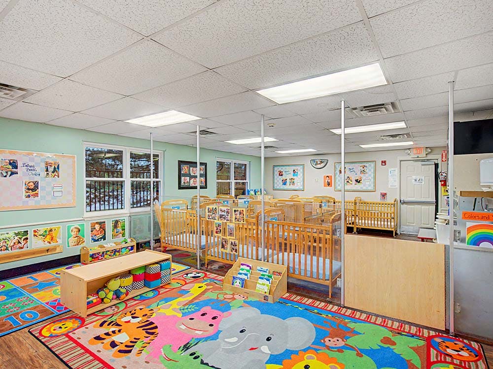 An infant room with multiple wooden cribs and colorful rugs