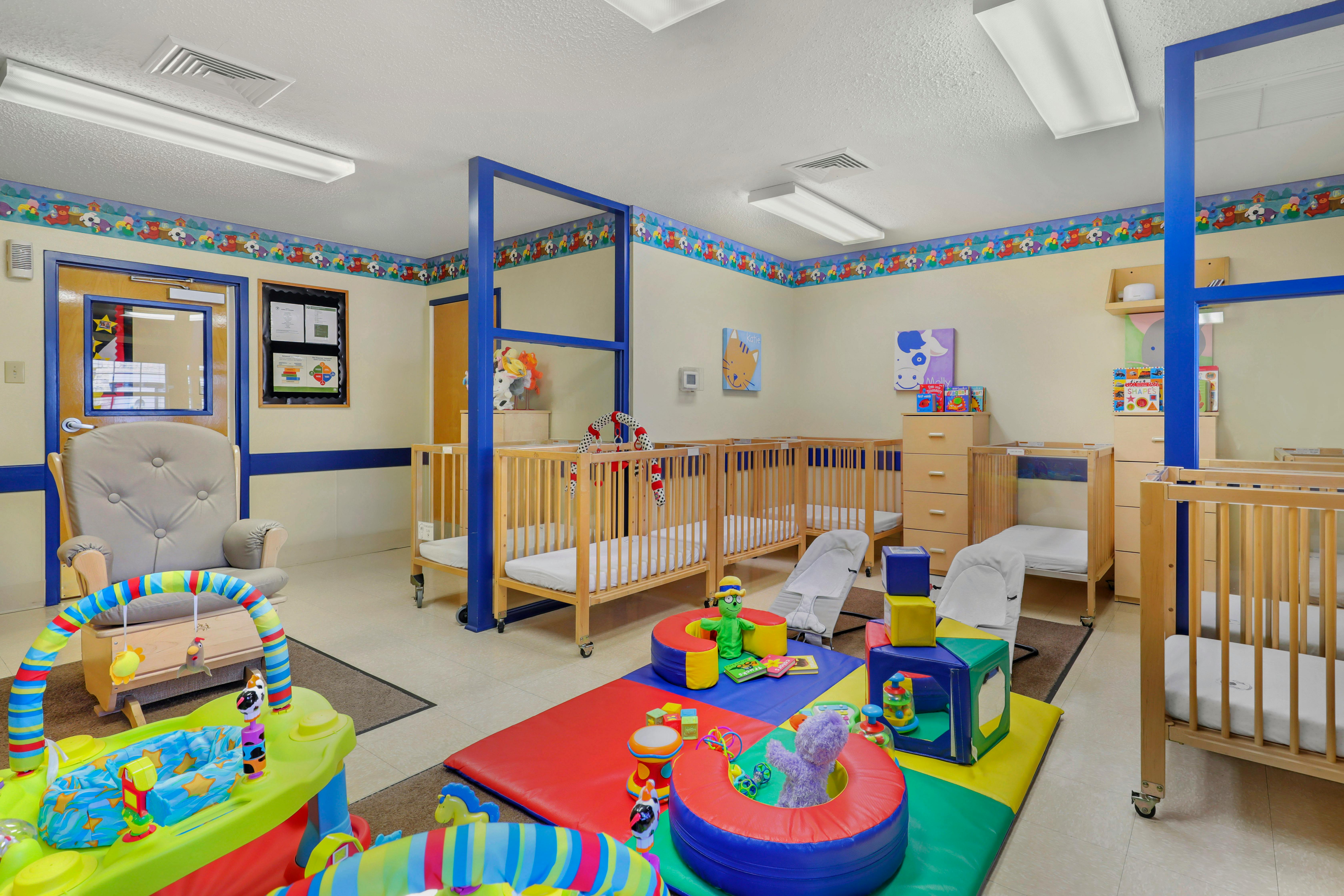 A colorful childcare room with cribs, playmats, and various infant toys