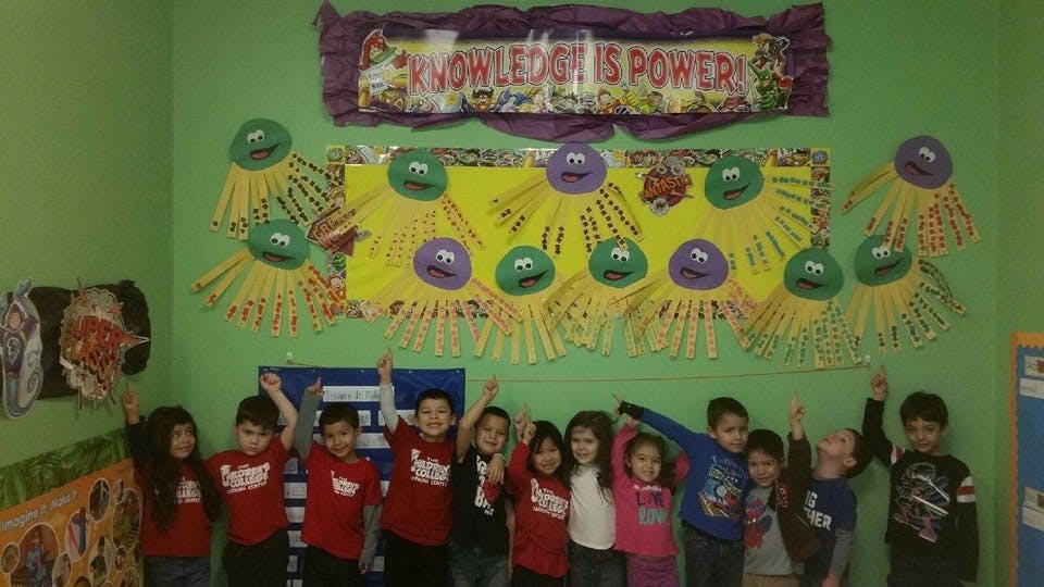 Group of children raising their hands in a classroom with a "Knowledge is Power" sign