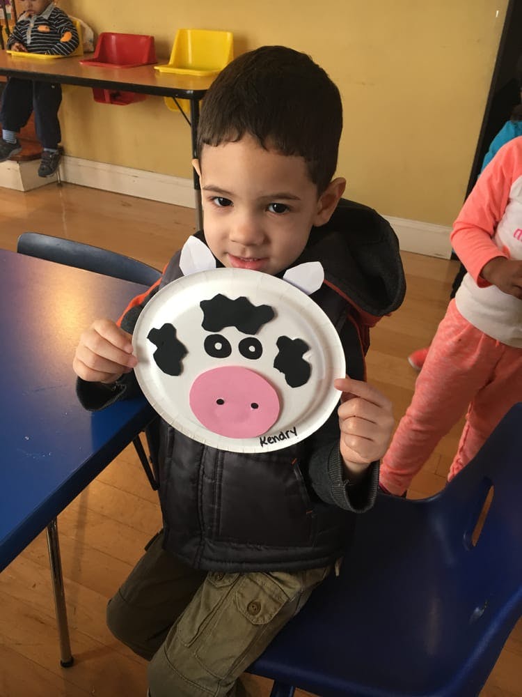Child holding up a paper plate craft of a cow face