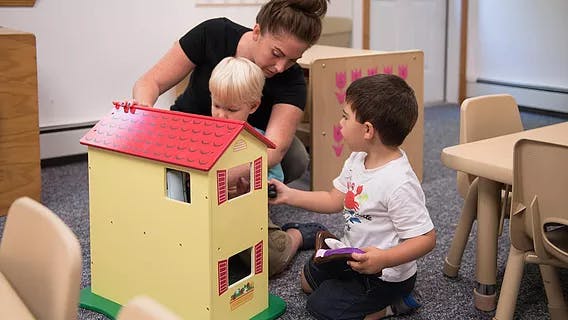Adult and two children playing with a dollhouse