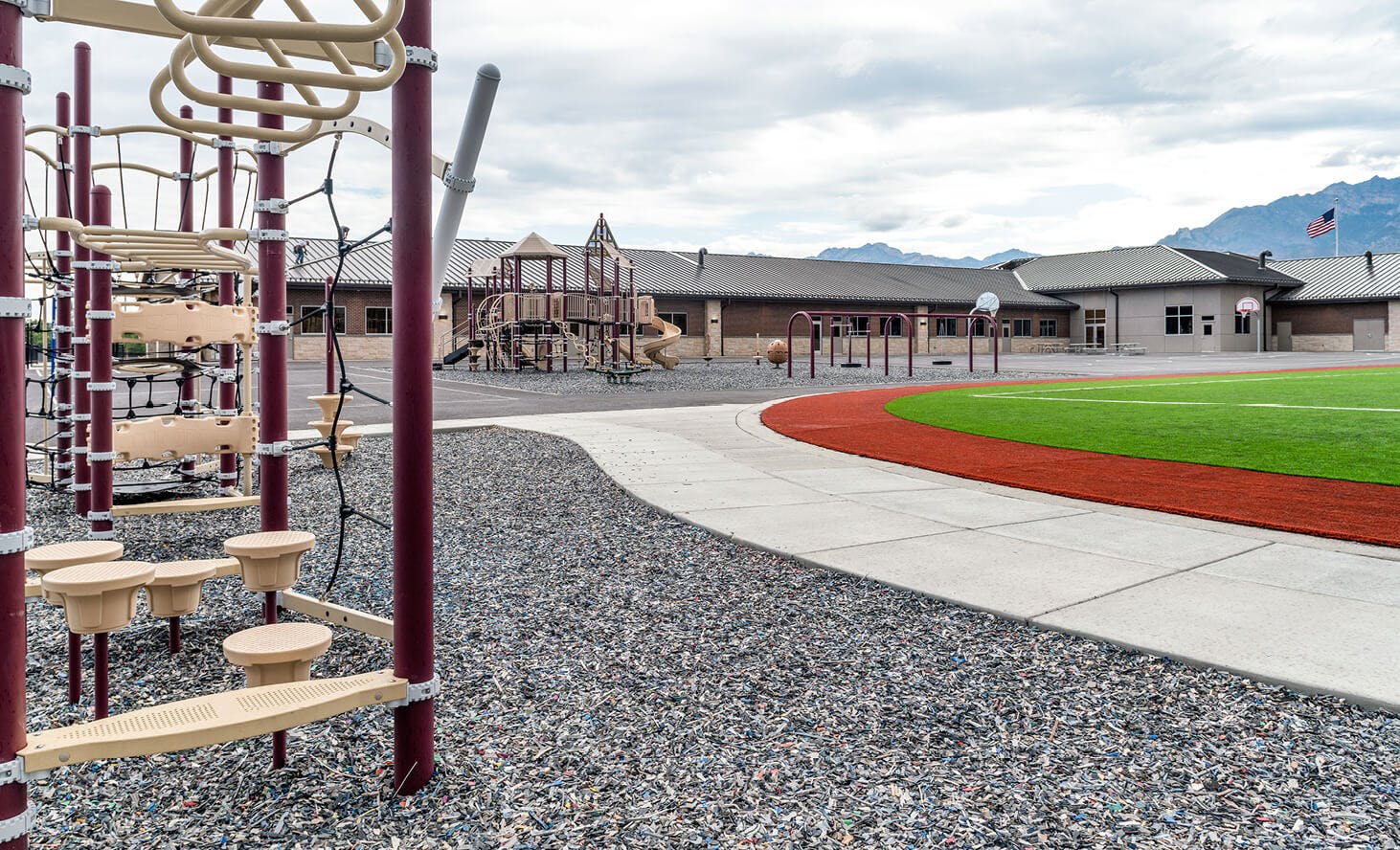 Playground equipment on gravel next to a track and school building