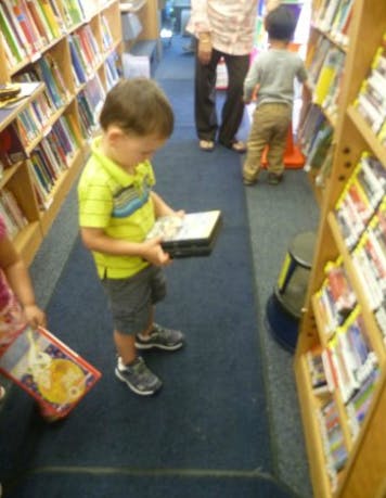 Child holding a book in a library aisle with bookshelves