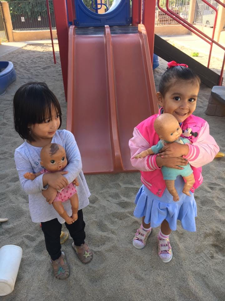 Two children holding dolls on a playground