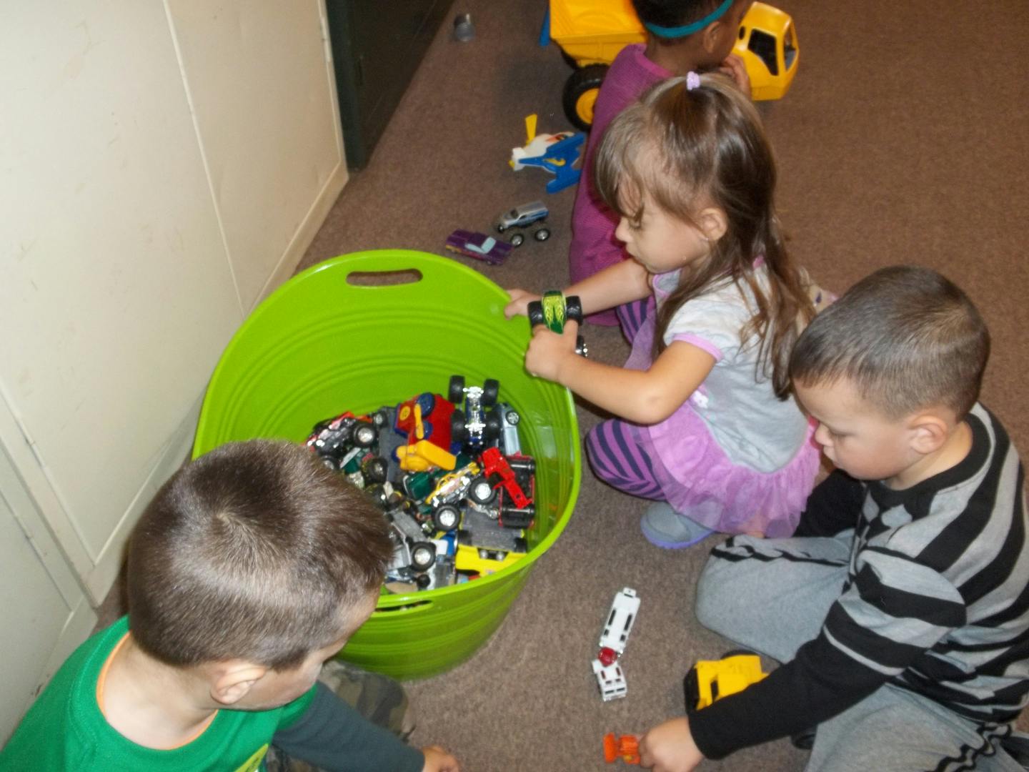 Children playing with toy cars from a green bin