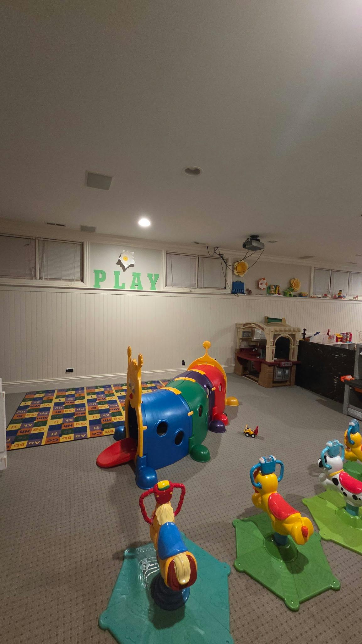 Indoor play area with colorful play tunnel and spring riders, with the word PLAY on the wall