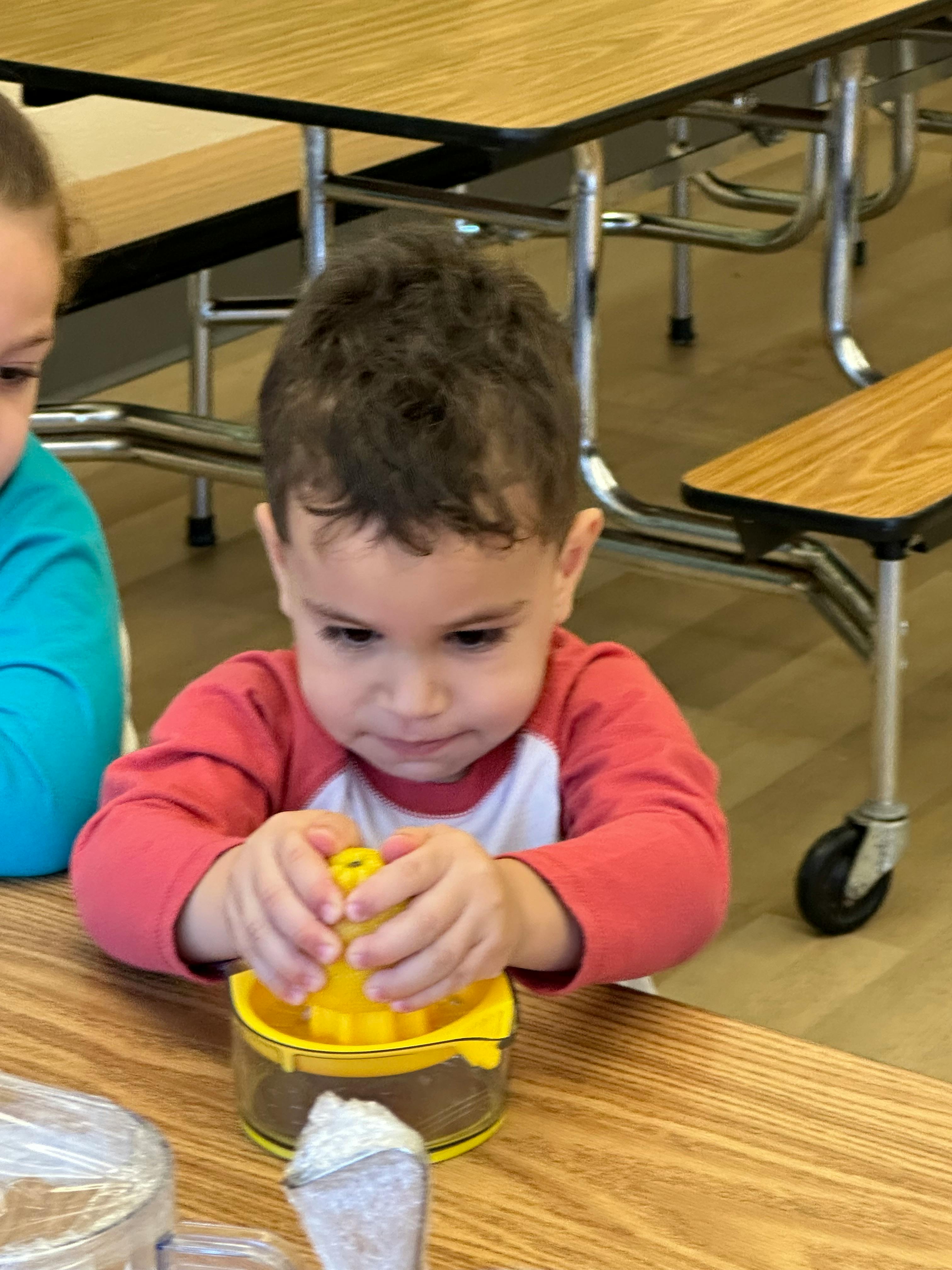 Child pressing down on a yellow juicer on a wooden table