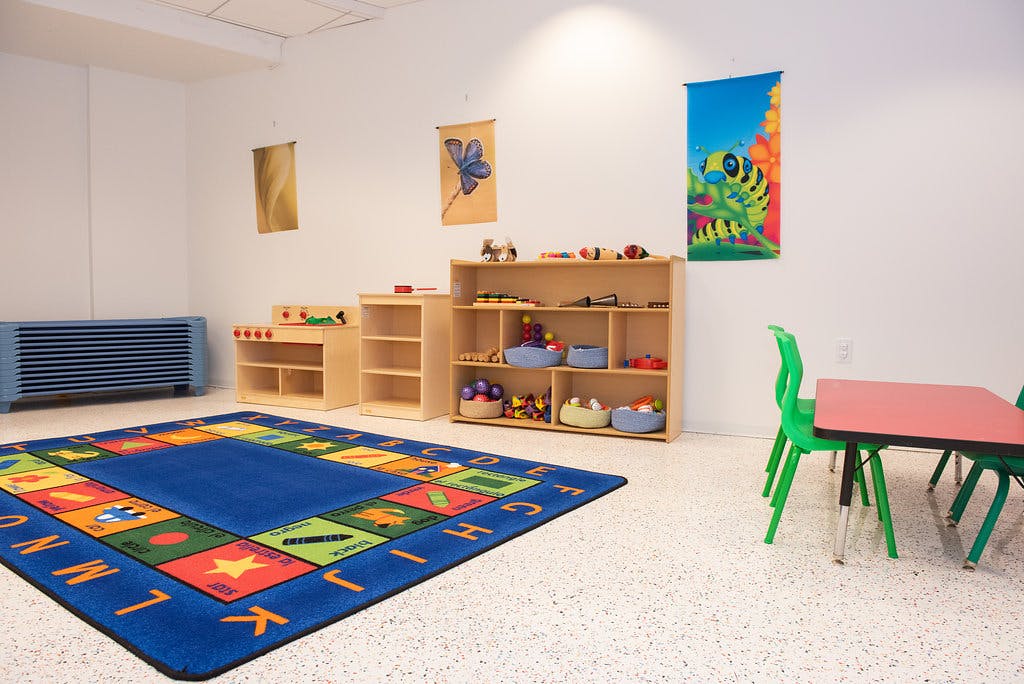 Classroom with an alphabet rug, cubbies, play kitchen, and small table with chairs
