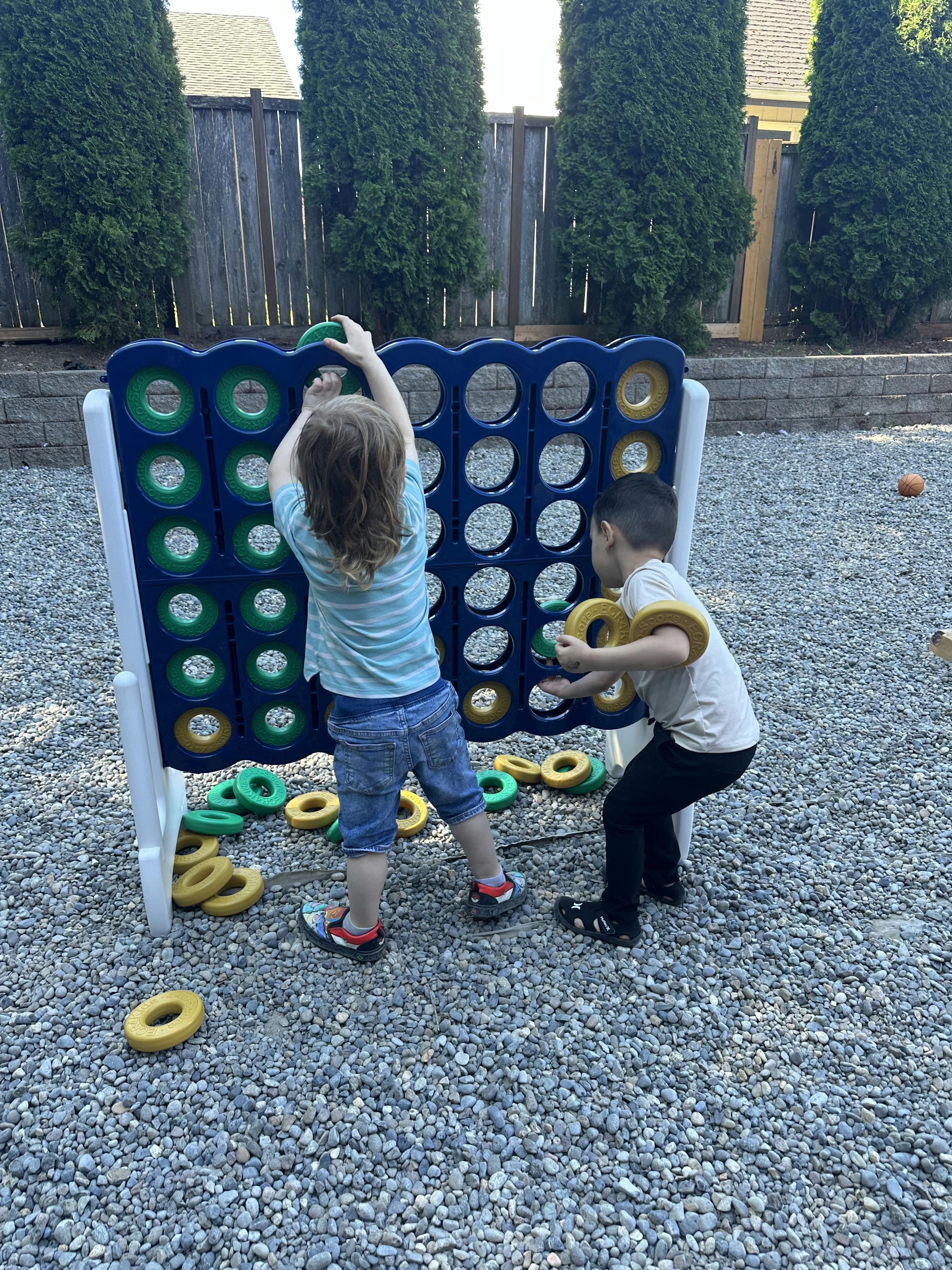 Two children playing a large vertical ring-toss game in a backyard