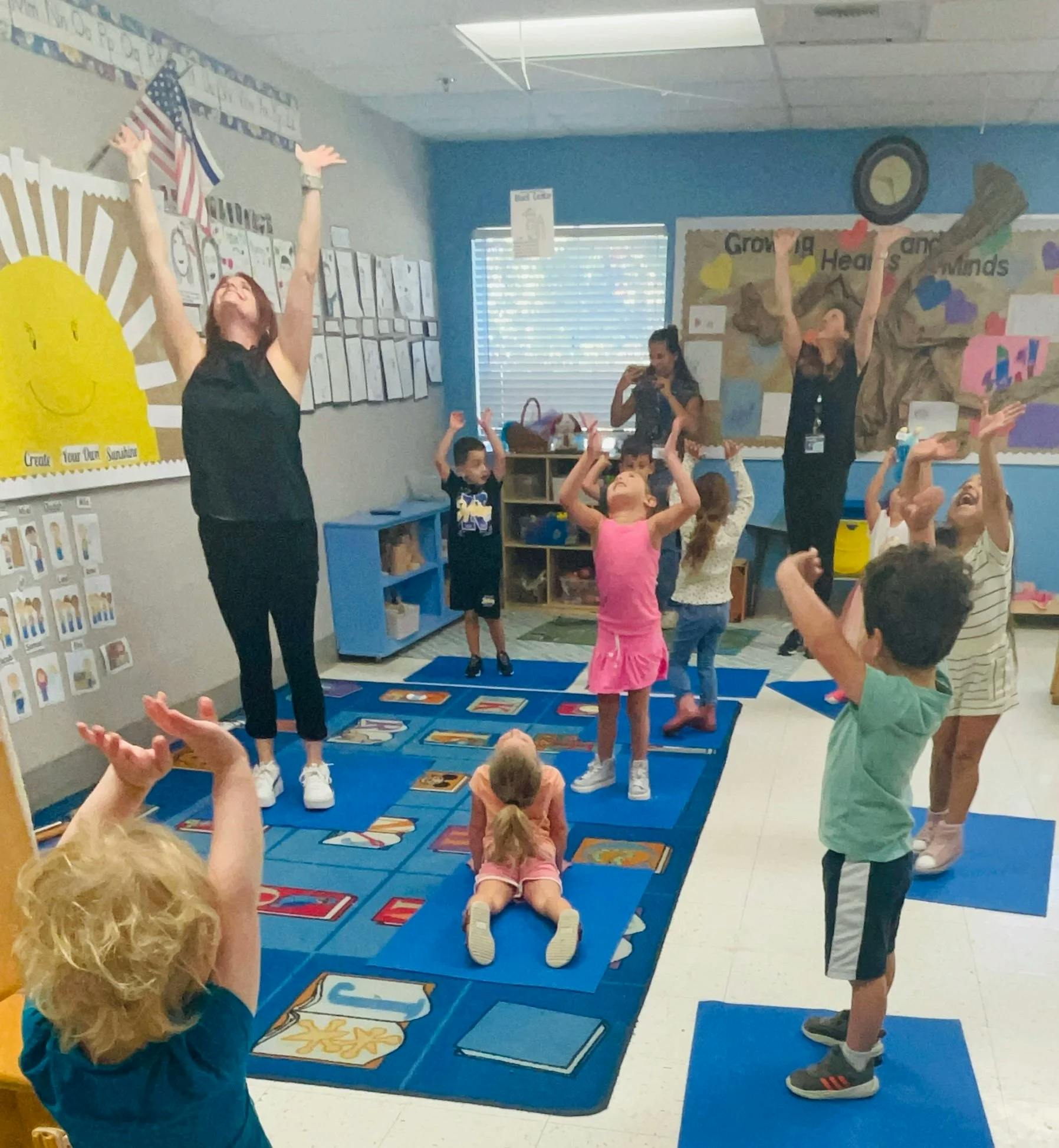 Teacher and children with arms raised in a classroom