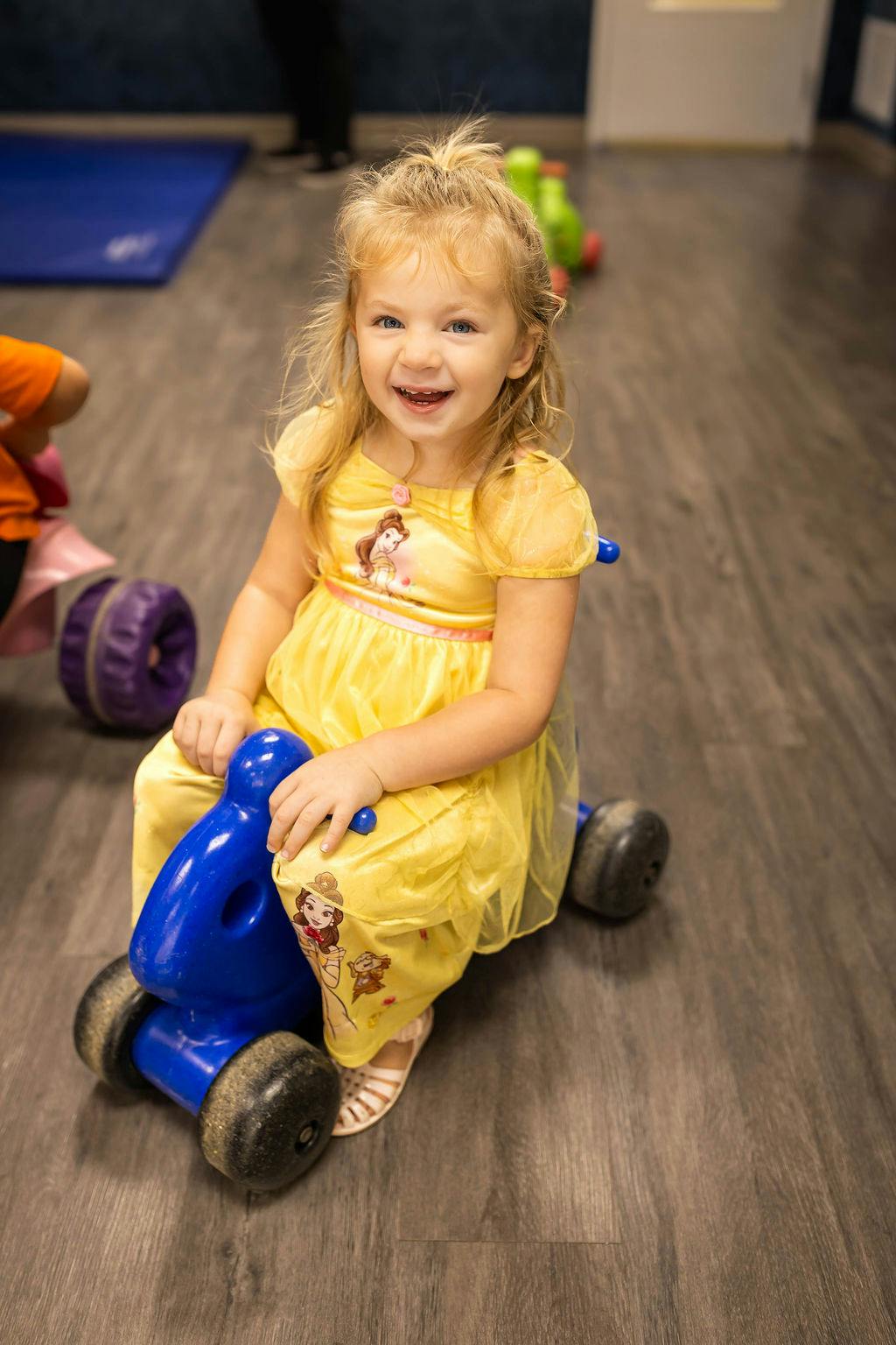 Child in a dress sitting on a toy ride-on vehicle