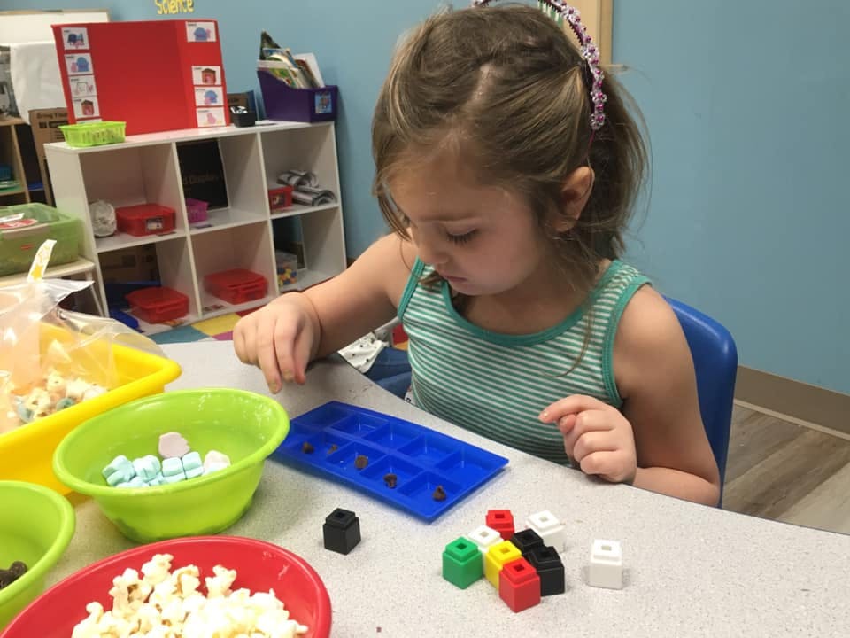 Child playing with small blocks and an ice cube tray at a table