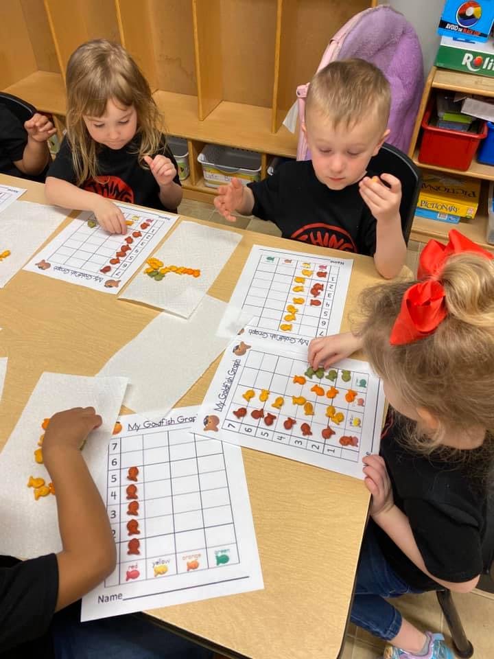 Children sorting goldfish crackers onto grid papers in classroom