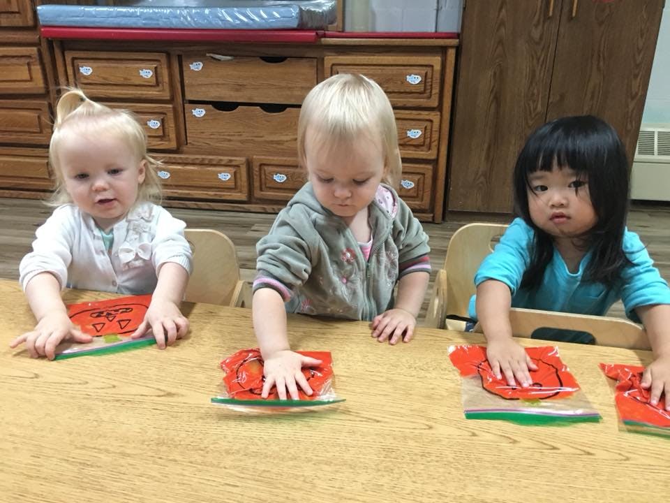 Three children sitting at a table with red craft materials