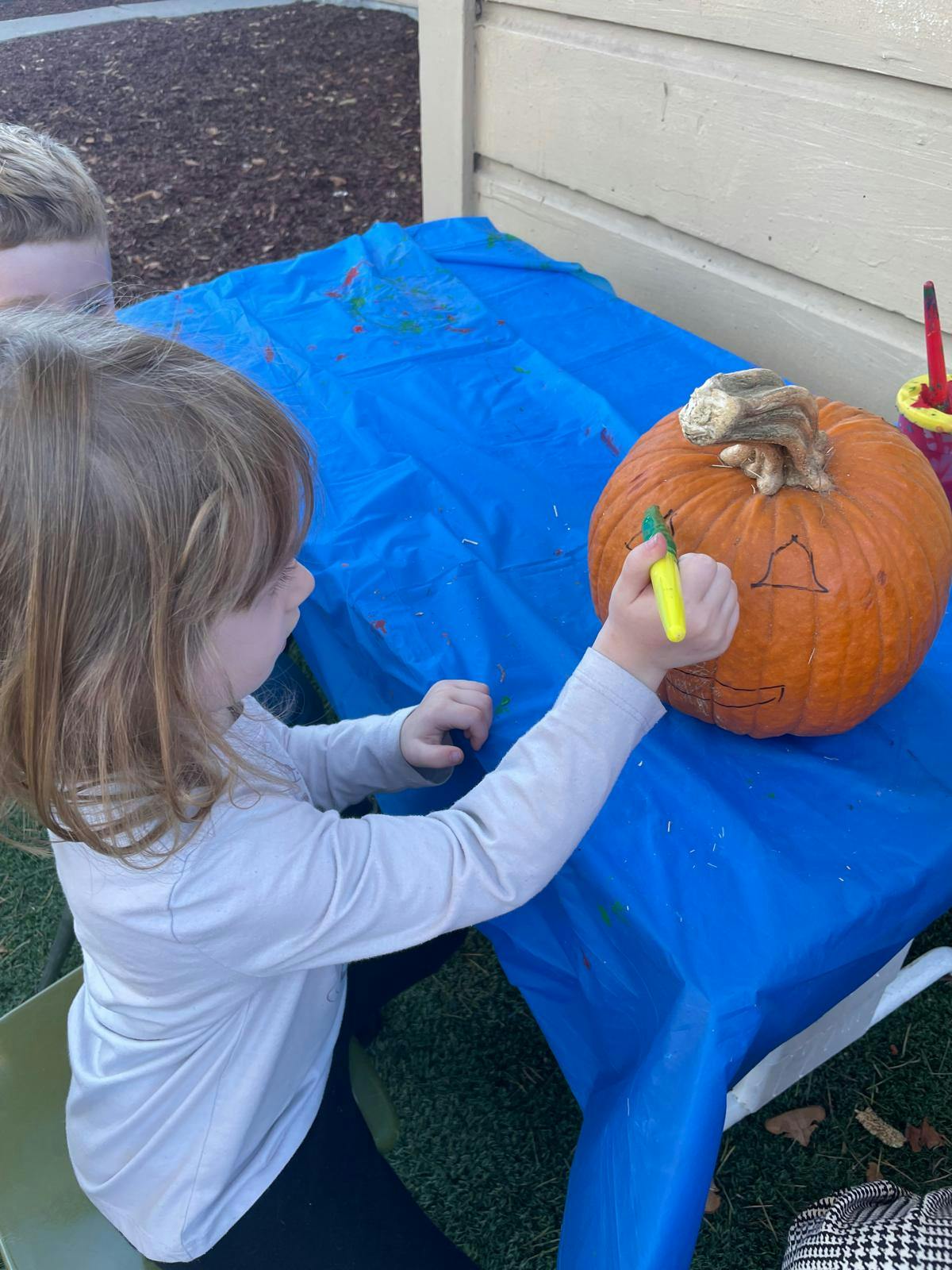 Child drawing a face on a pumpkin with a marker at a table