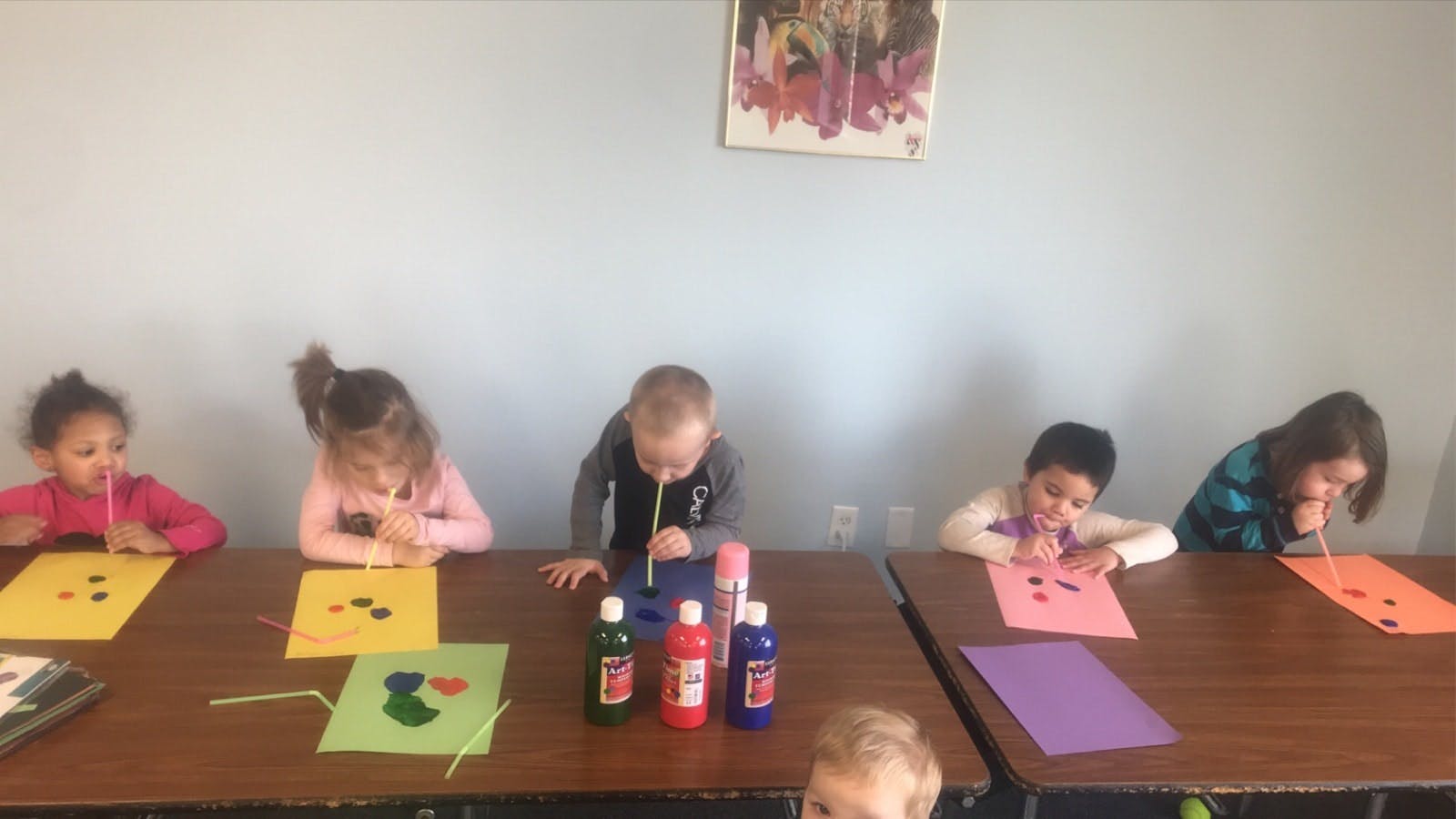 Children sitting at tables doing an art activity with straws and paint