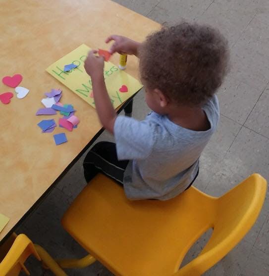 Child making a craft with paper cutouts and glue at a table