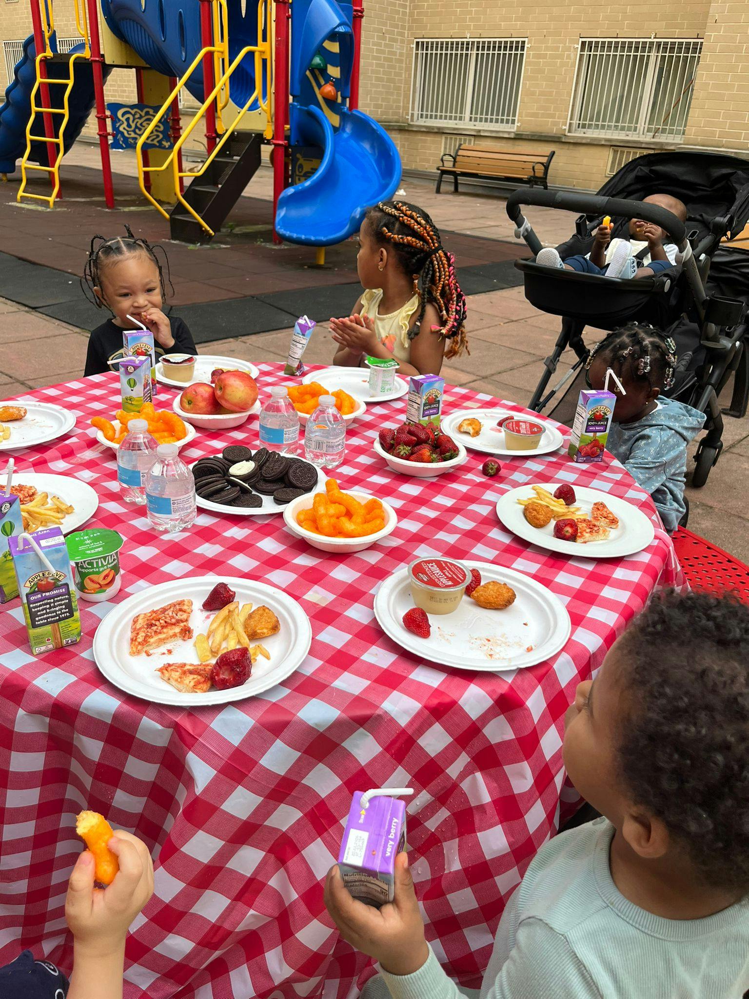 Children eating snacks and drinking juice at a table on a playground