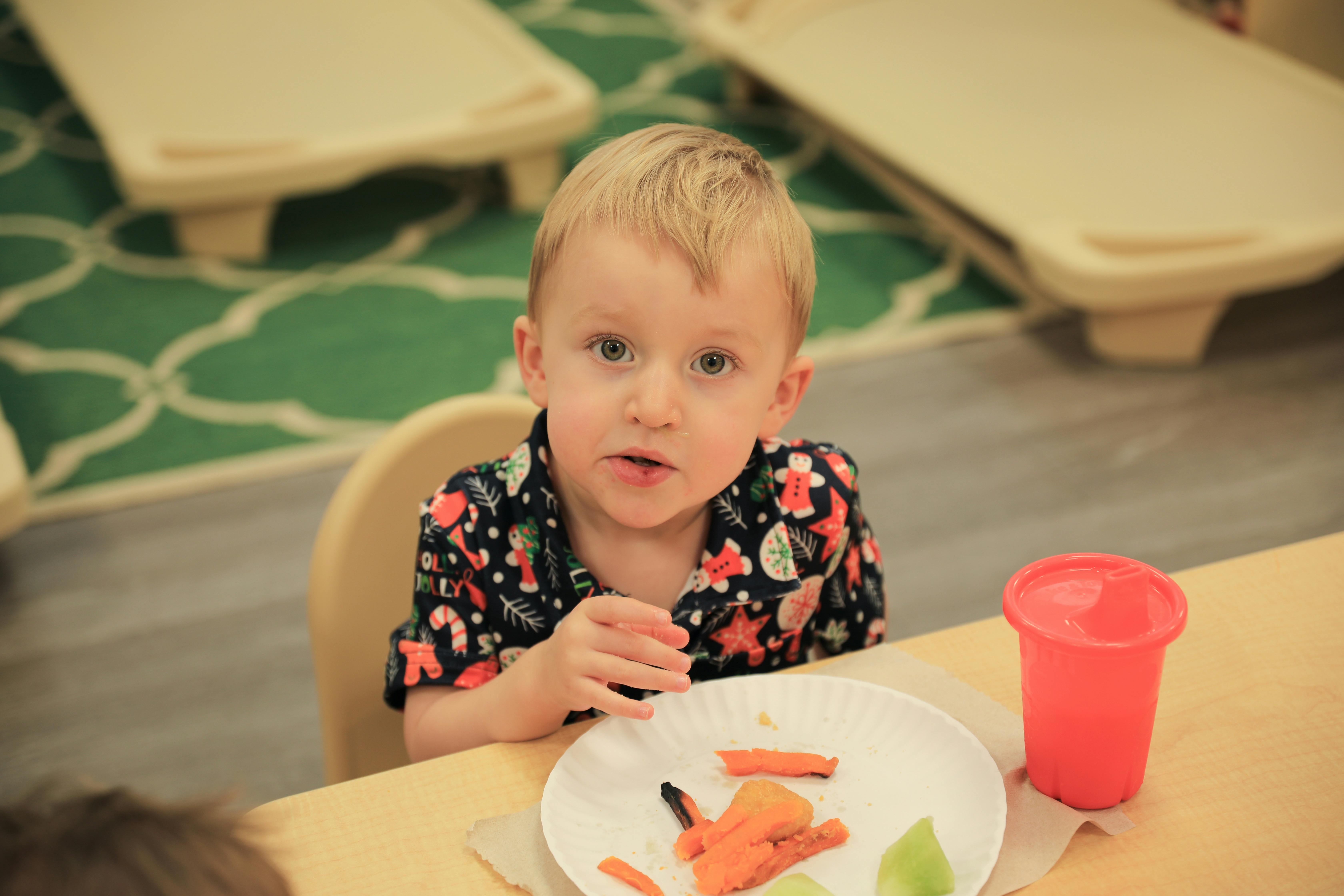Child sitting at a table with a plate of food and a cup