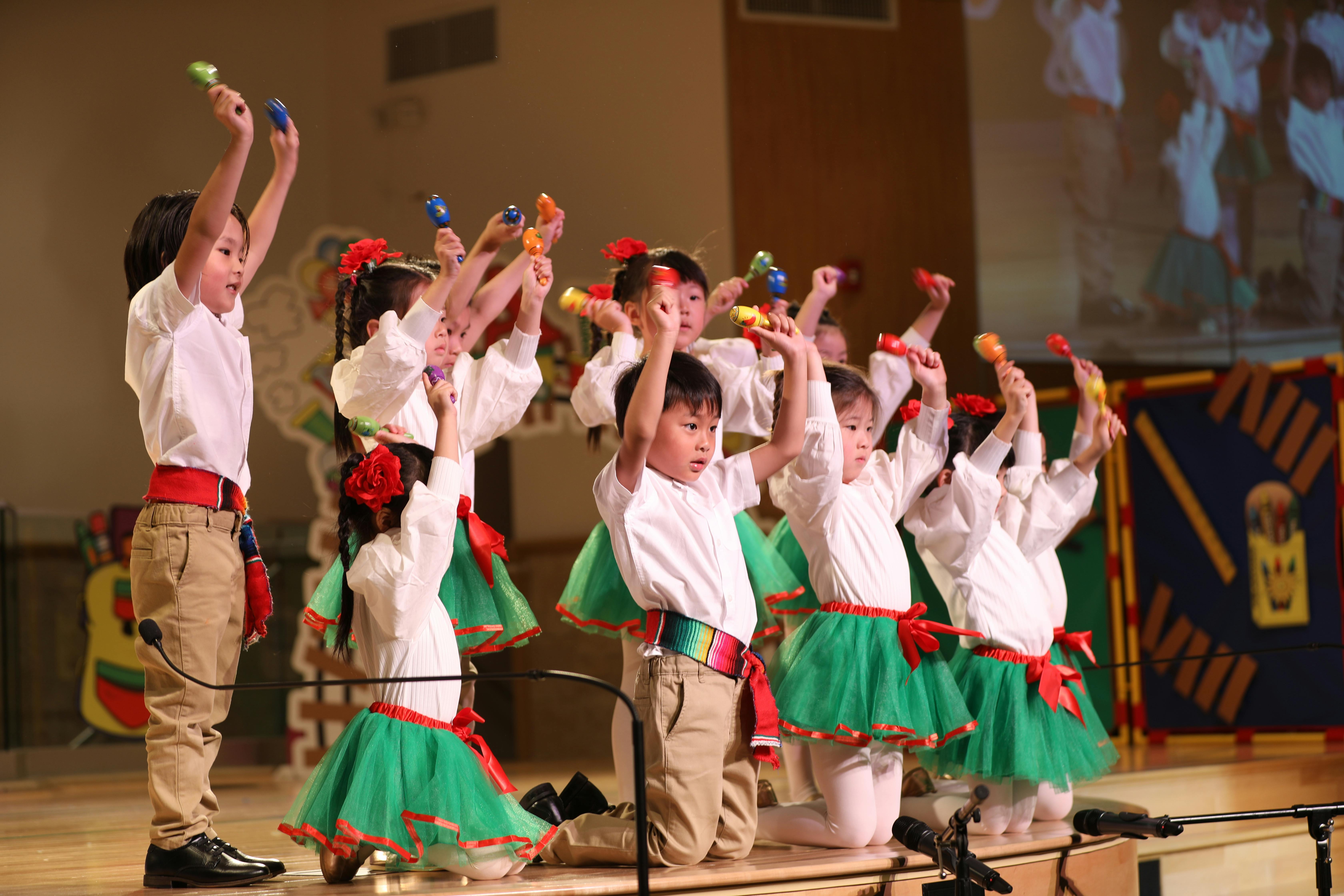 Children in costumes holding maracas with arms raised