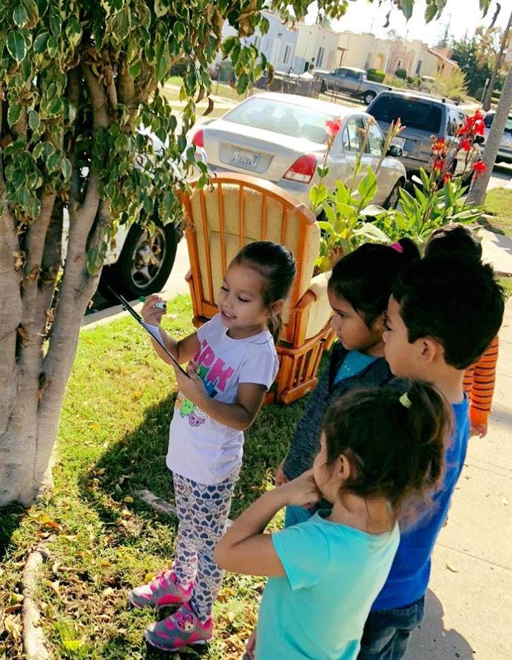 Child holding a tablet next to a tree with other children watching