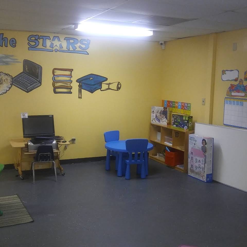 Classroom with a laptop on a desk, a small blue table with chairs, and shelves