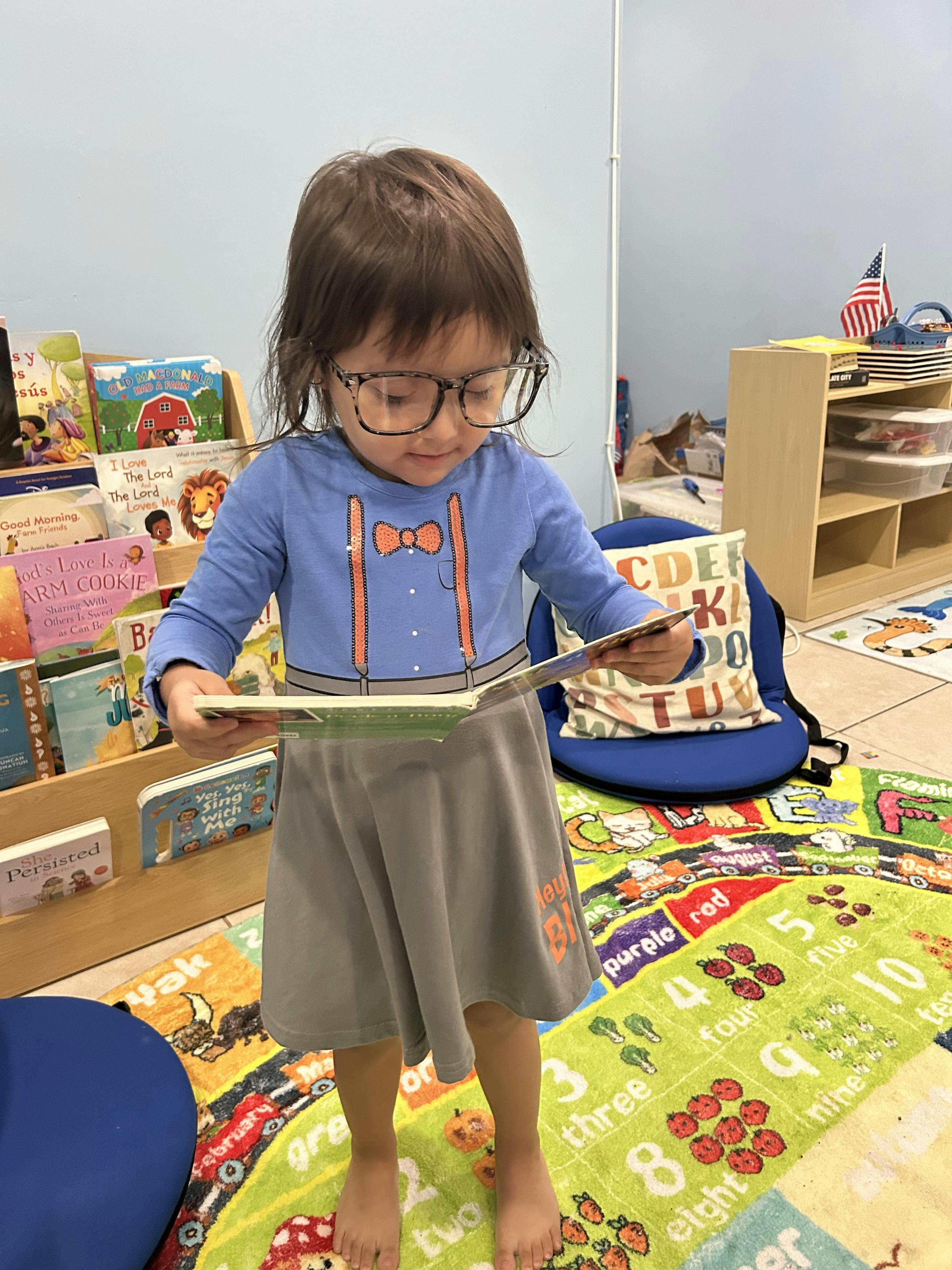 Child in glasses looking down at a book in their hands