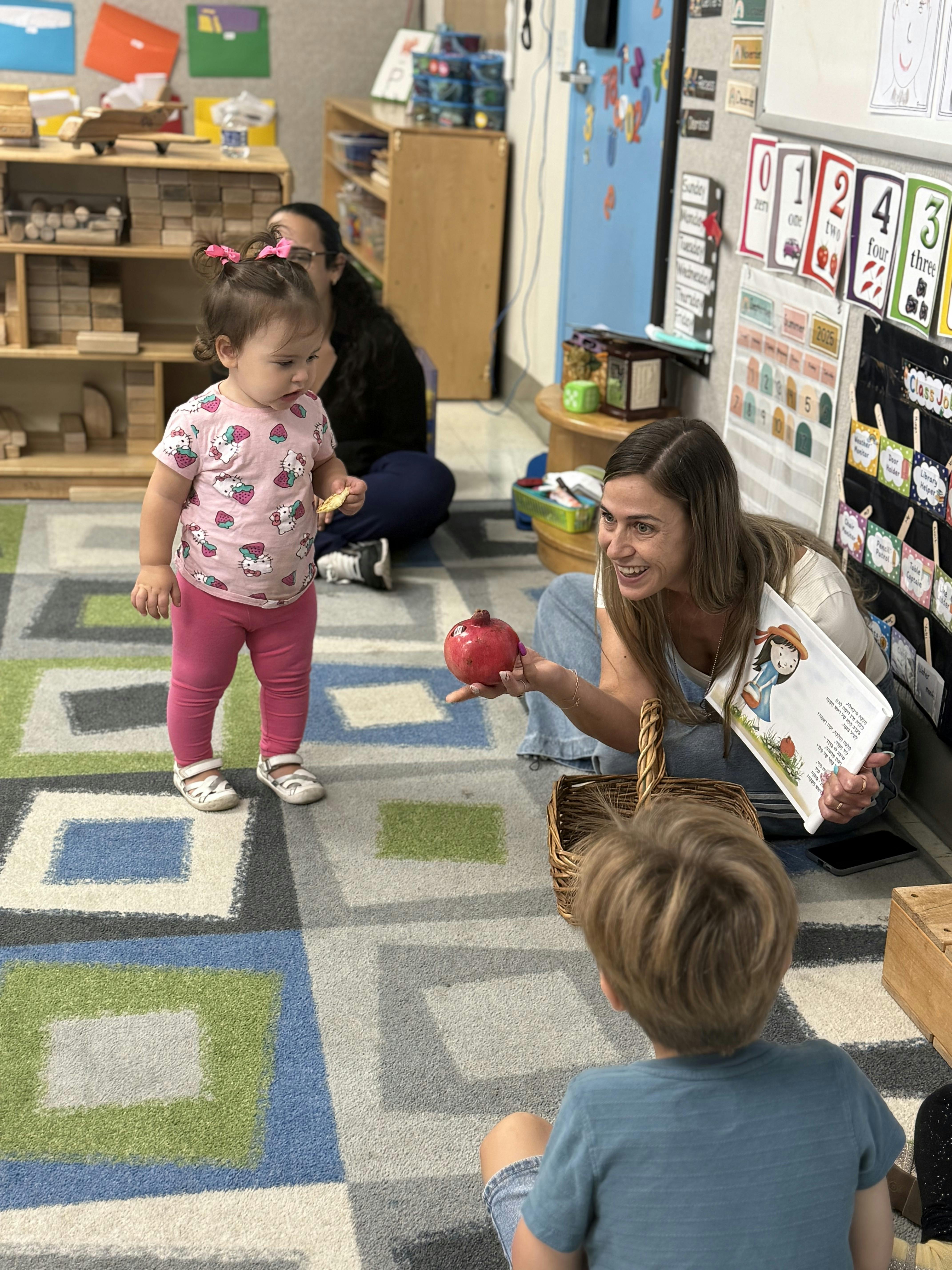 Teacher holding a pomegranate and book for children in a classroom