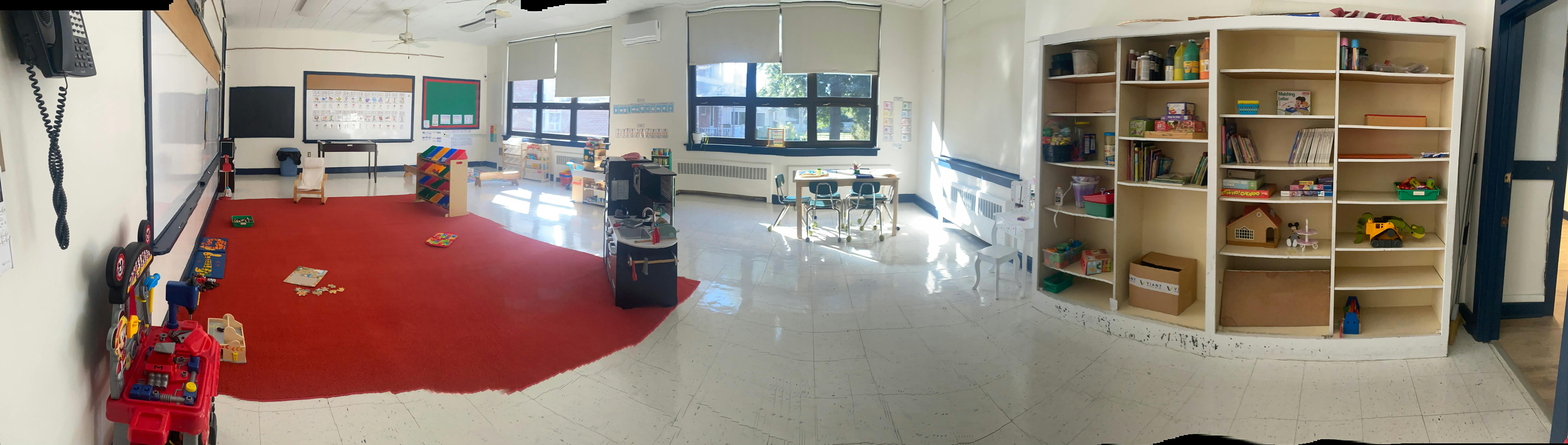 Classroom with red rug, tables, chairs, and shelves
