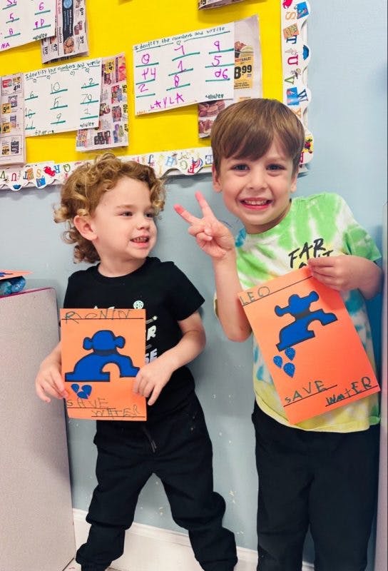 Two children holding up orange papers with blue faucet cutouts