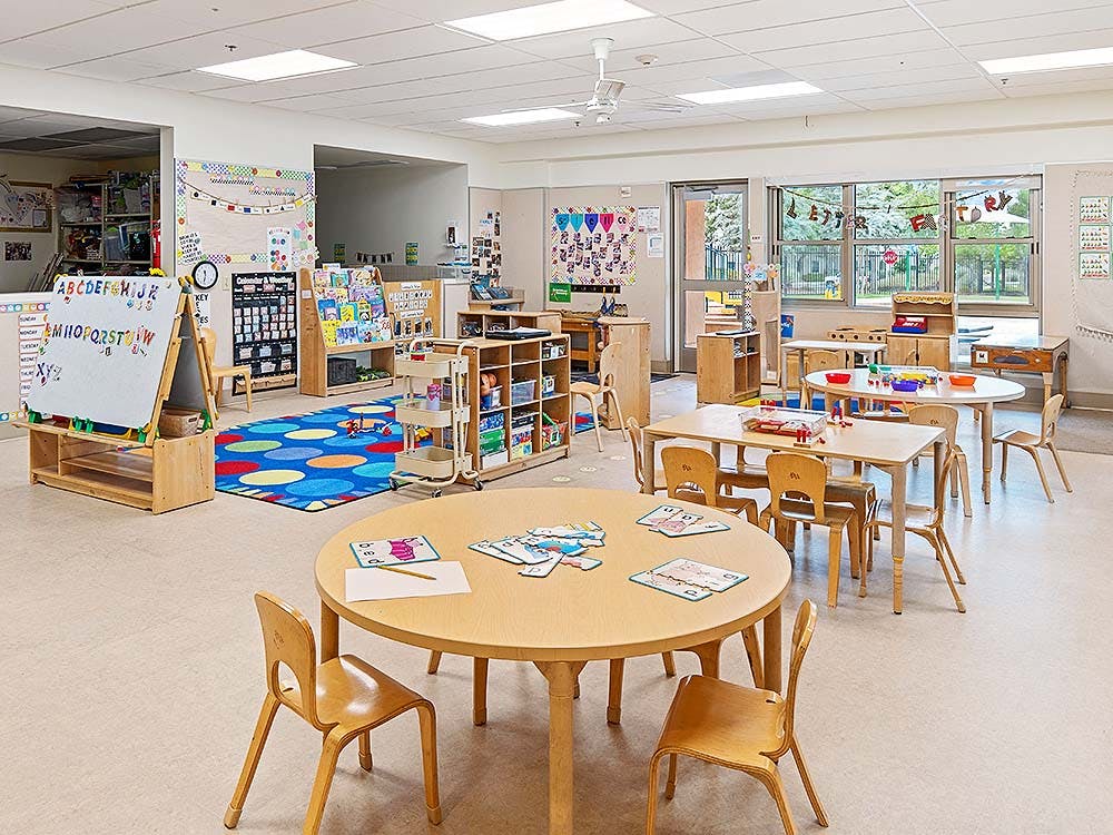 Classroom with small wooden tables and chairs, a colorful rug, and alphabet board