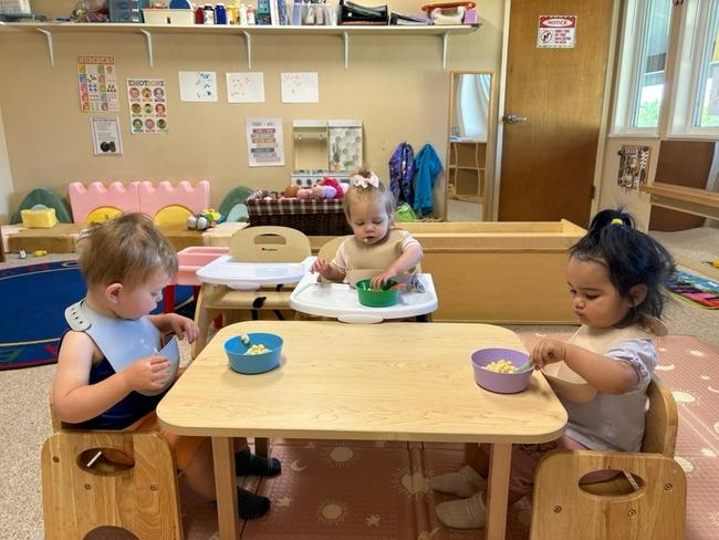Three children eating from bowls at a table in a classroom