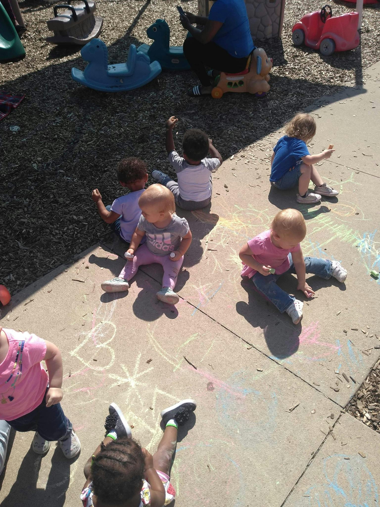 Children sitting on pavement drawing with chalk