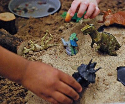 Child's hands playing with dinosaur toys in sand