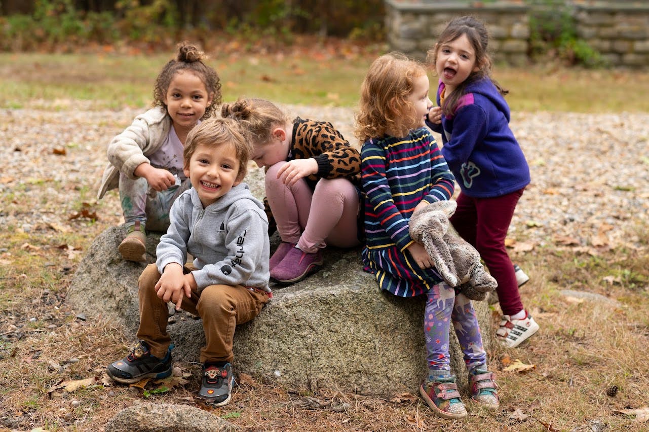 Group of children sitting and playing on a large rock outdoors