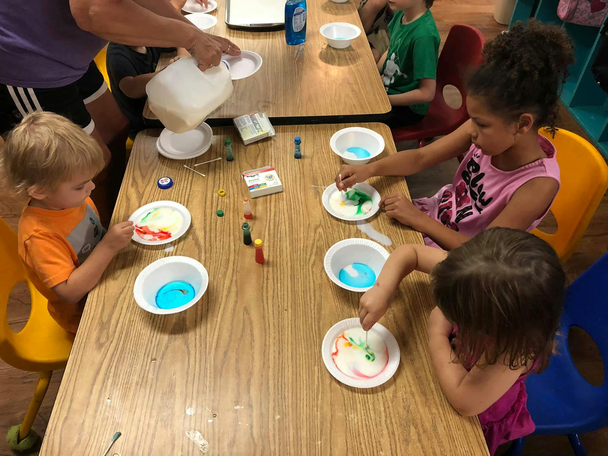 Children at a table doing an art activity with paint and bowls