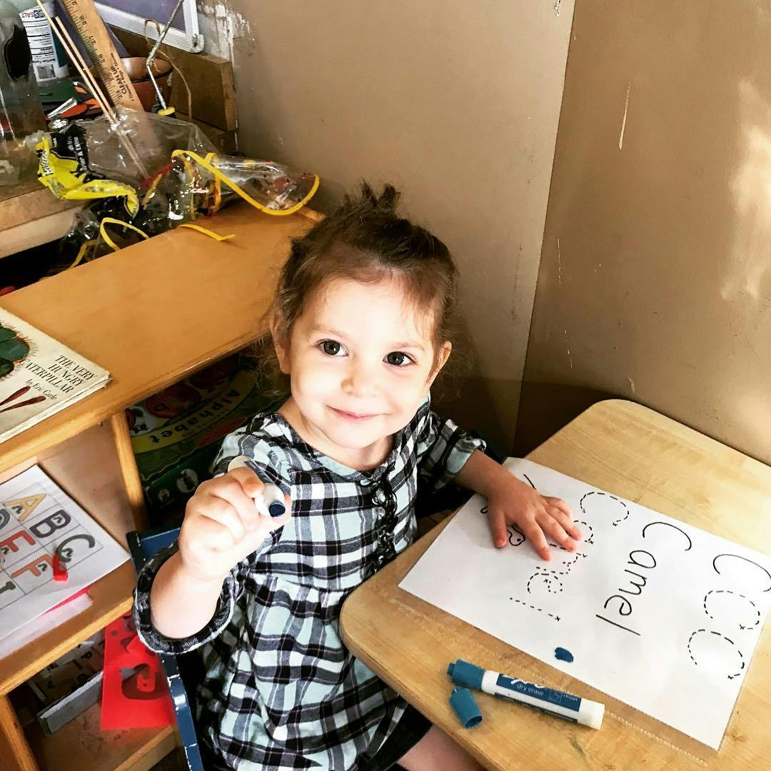 Child holding a marker and sitting at a desk with a paper