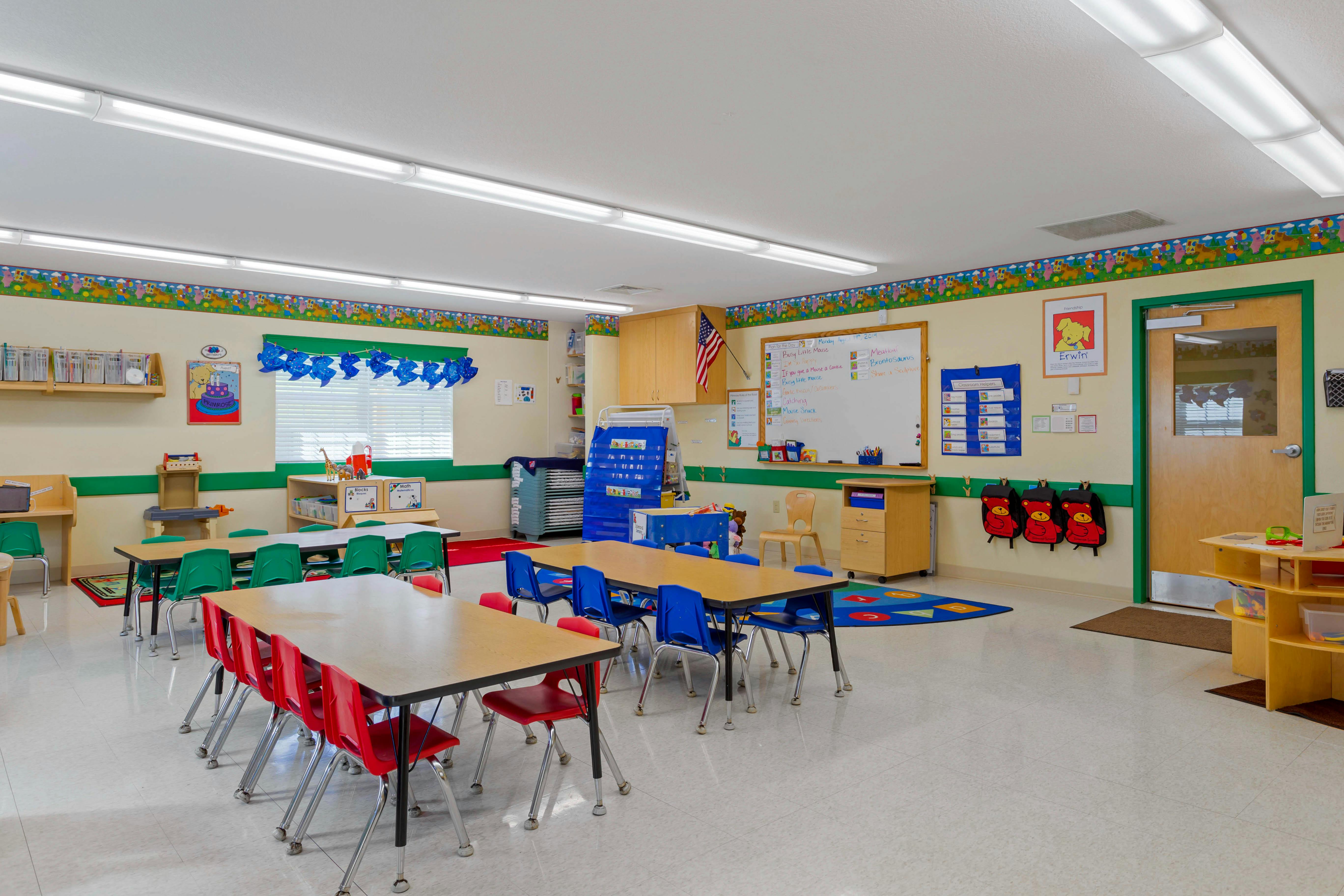 Empty classroom with multiple tables and chairs, whiteboards, and cubbies