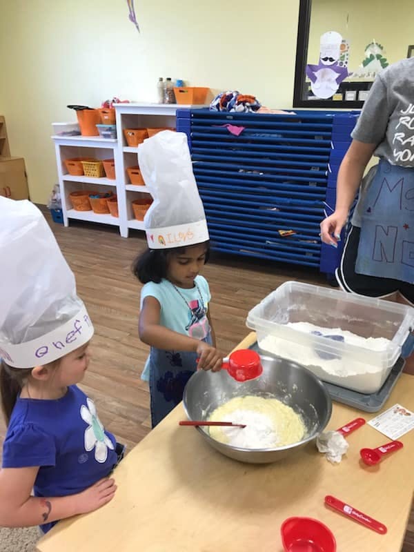 Two children in chef hats mixing ingredients in a bowl