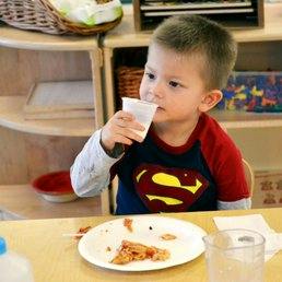 Child in Superman shirt drinking from a cup at a table with a plate of food