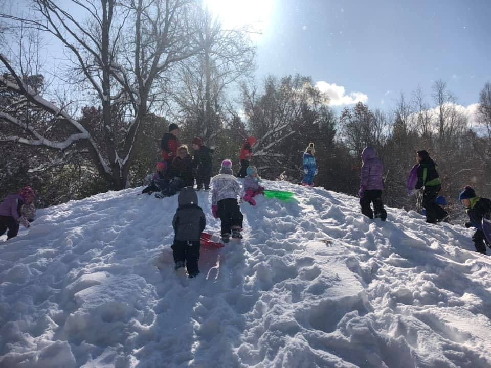 People and children on a snowy hill with sleds