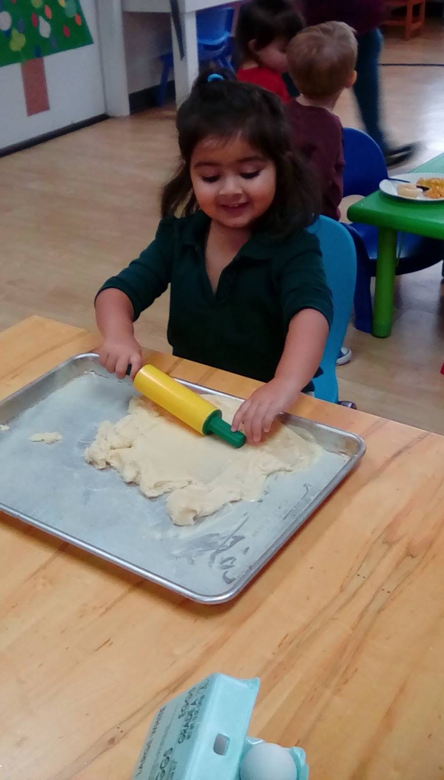 Child rolling dough on a baking sheet with a toy rolling pin