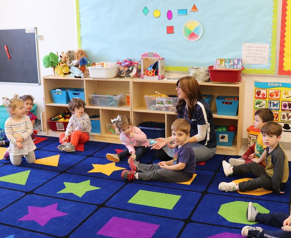 Adult and children sitting on a colorful rug in a classroom