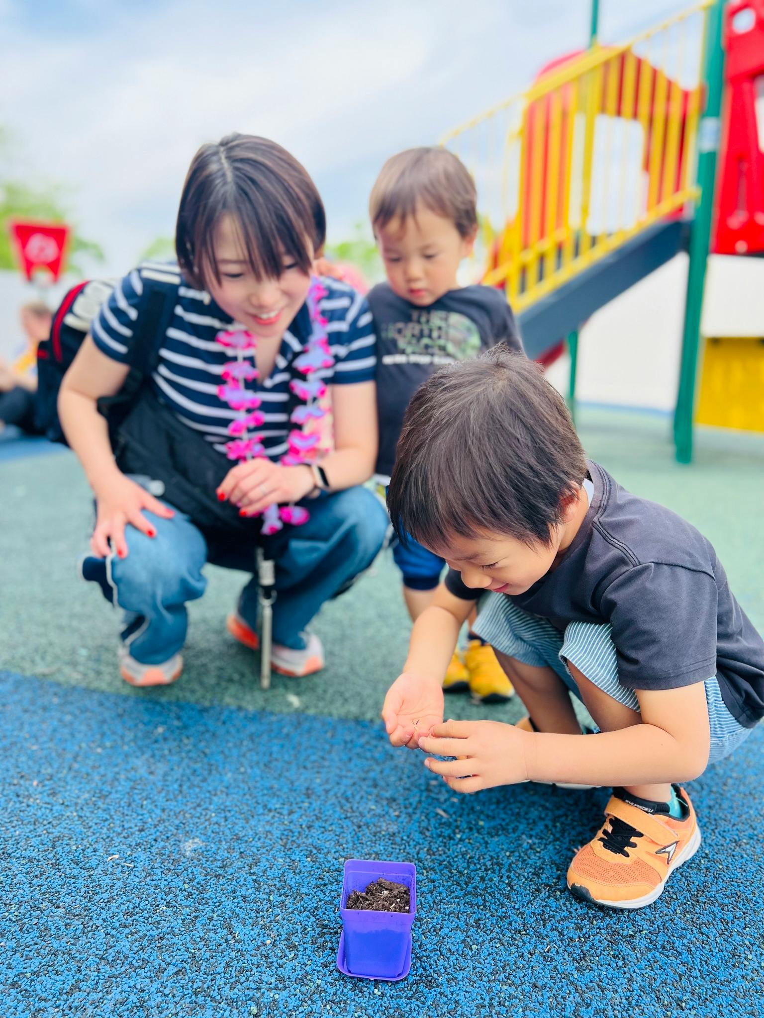 Person and two children crouching, looking at a small purple container