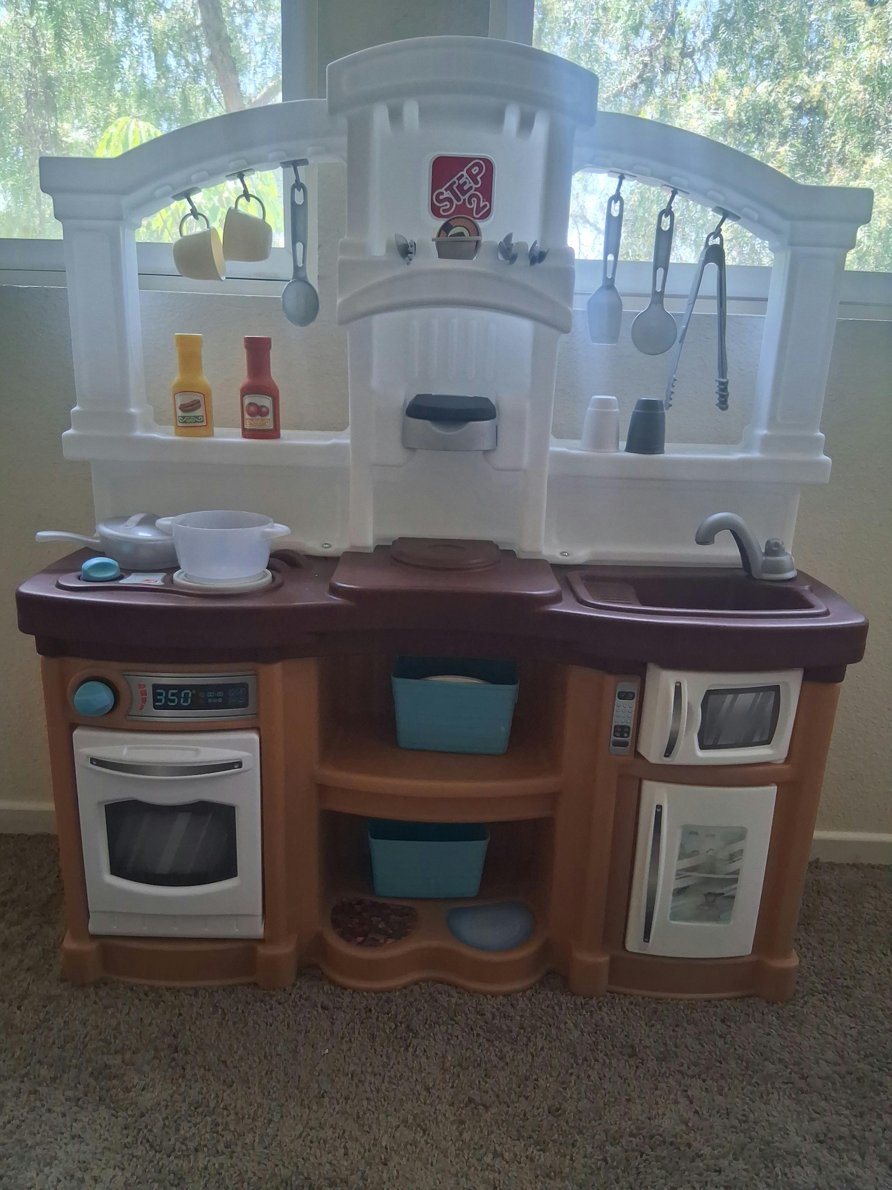 Child's toy kitchen with utensils, cups, and play food bottles